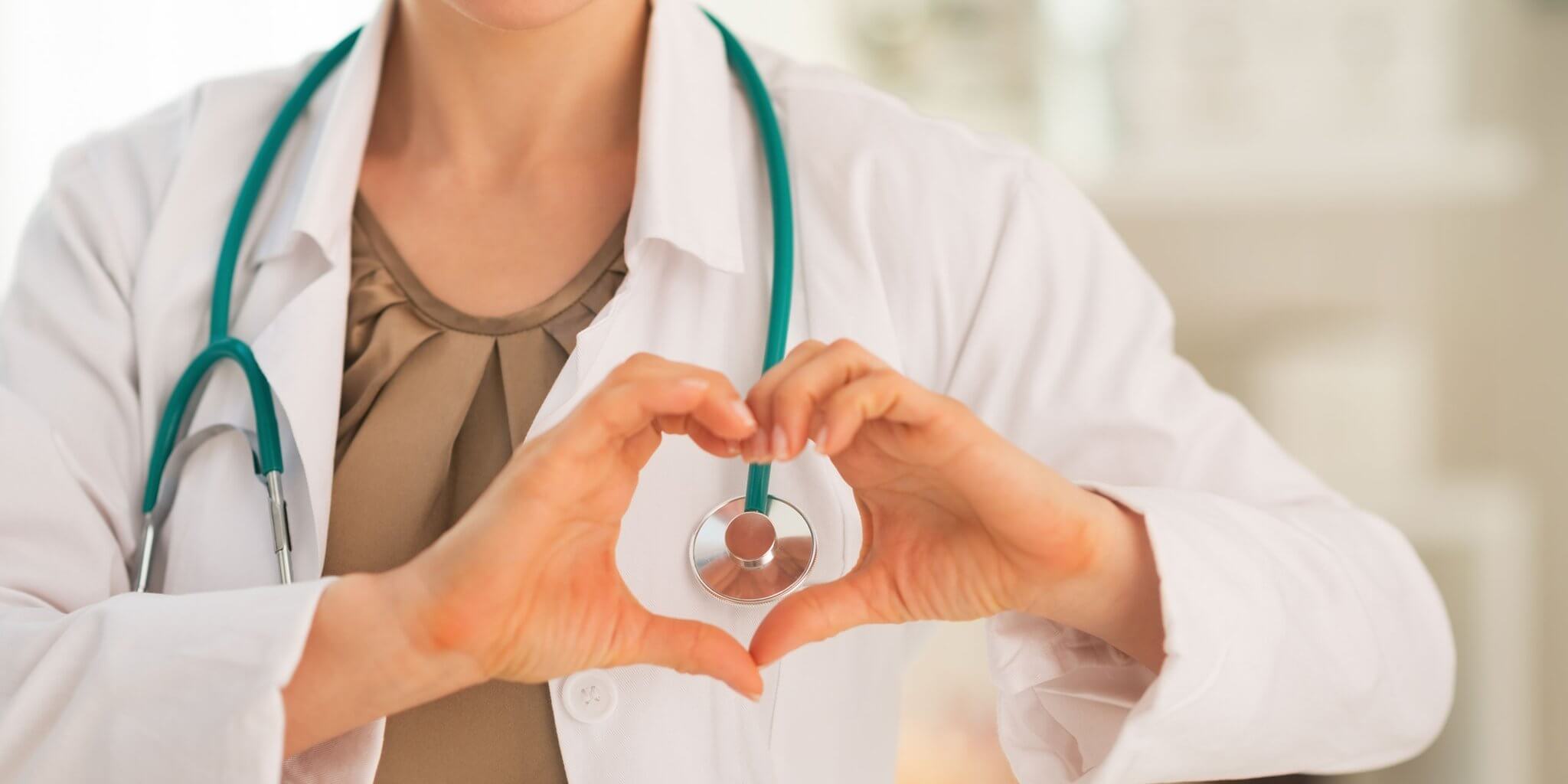 Image of female doctor wearing lab coat and stethoscope holding hands in a heart
